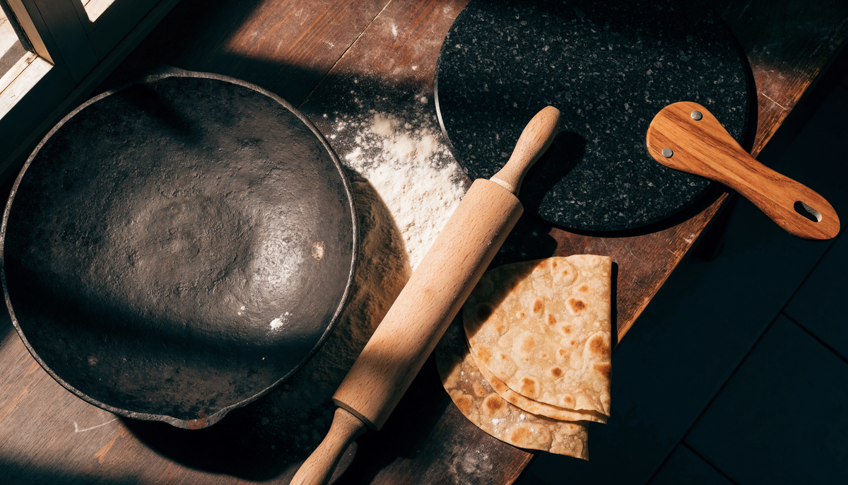 Old cast iron tawa next to a granite non-stick tawa with wooden handle